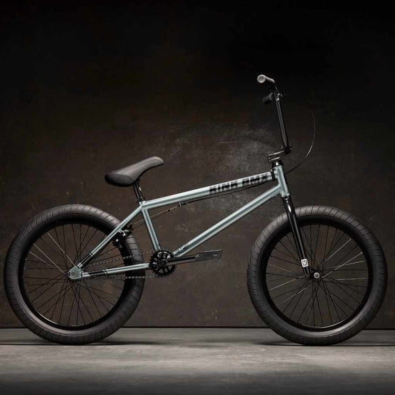 Side view of Kink Whip XL 20 inch BMX bike in slate grey photographed in an industrial warehouse