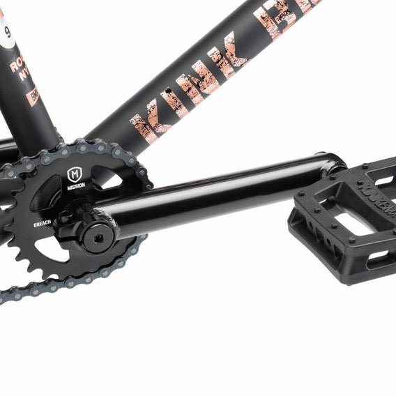 Close up of drive chain on Kink Gap BMX bike in midnight black, photo shows Mission Breach 25 tooth sprocket, Mission Triumph Chromoly 3 piece cranks and Kink Hemlock plastic pedal