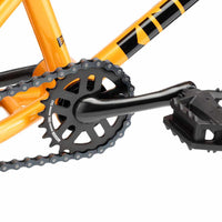 Close up photo of the drive train of a Kink Roaster 12 inch orange BMX bike showing the black Mission Coil 24 tooth sprocket, one piece cranks and plastic pedal