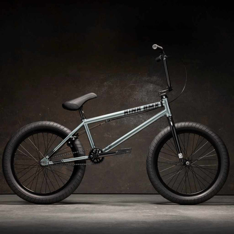 Side view of Kink Whip XL 20 inch BMX bike in slate grey photographed in an industrial warehouse