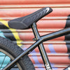 Close-up of a black bicycle seat and frame against a colorful corrugated metal background
