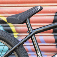 Close-up of a black bicycle seat and frame against a colorful corrugated metal background