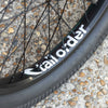 Close-up of a bicycle wheel with 'tall order' branding on a textured surface.