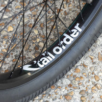 Close-up of a bicycle wheel with 'tall order' branding on a textured surface.