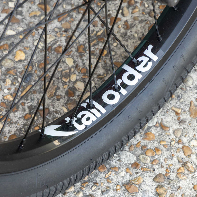 Close-up of a bicycle wheel with 'tall order' branding on a textured surface.