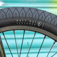 Close-up of a bicycle tire with 'Matt Ray Designer' branding on a blurred background