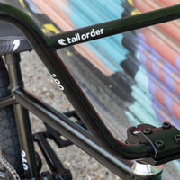 Close-up of a bicycle frame with 'tall order' branding against a blurred background.