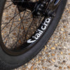 Close-up of a bicycle wheel with 'Tall Order' branding on a textured pavement.