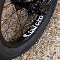 Close-up of a bicycle wheel with 'Tall Order' branding on a textured pavement.