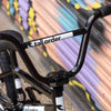 Close-up of a tall order bmx handlebar with 'tall order' branding against a colorful mural background.